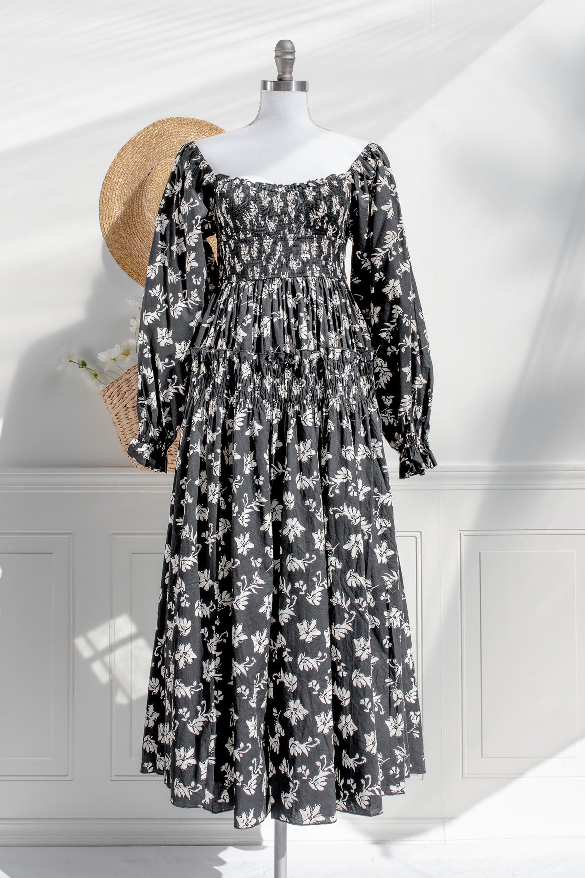 Black floral dress on a mannequin with a straw hat against a white wall