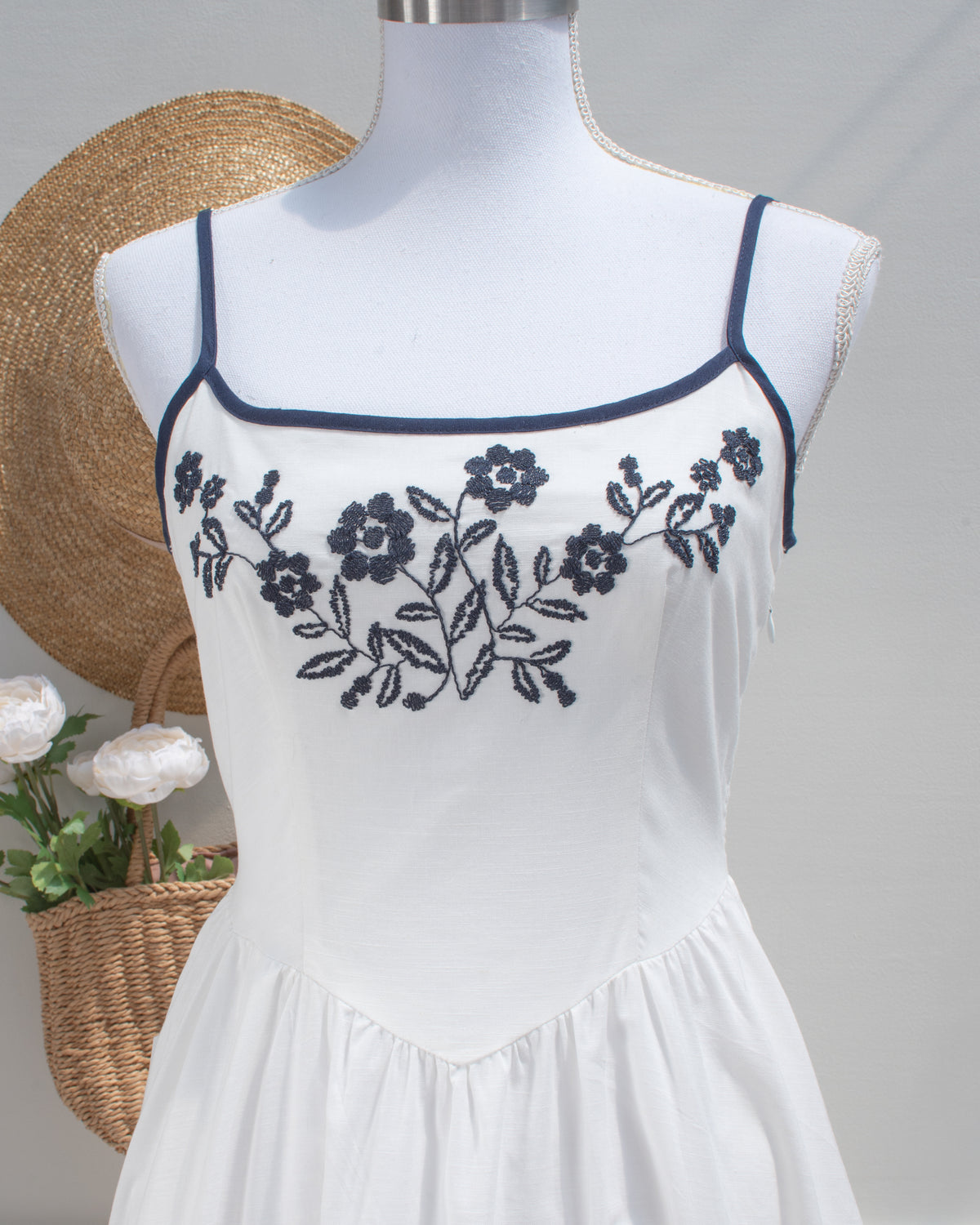 Close-up of navy floral embroidery and trim at the neckline of the white embroidered dress.