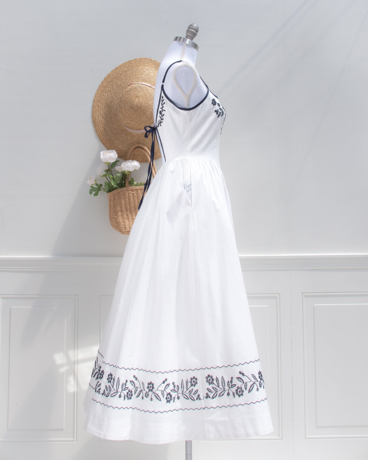 Side view of the white embroidered dress, showing the navy tie, full skirt and embroidered hem border.