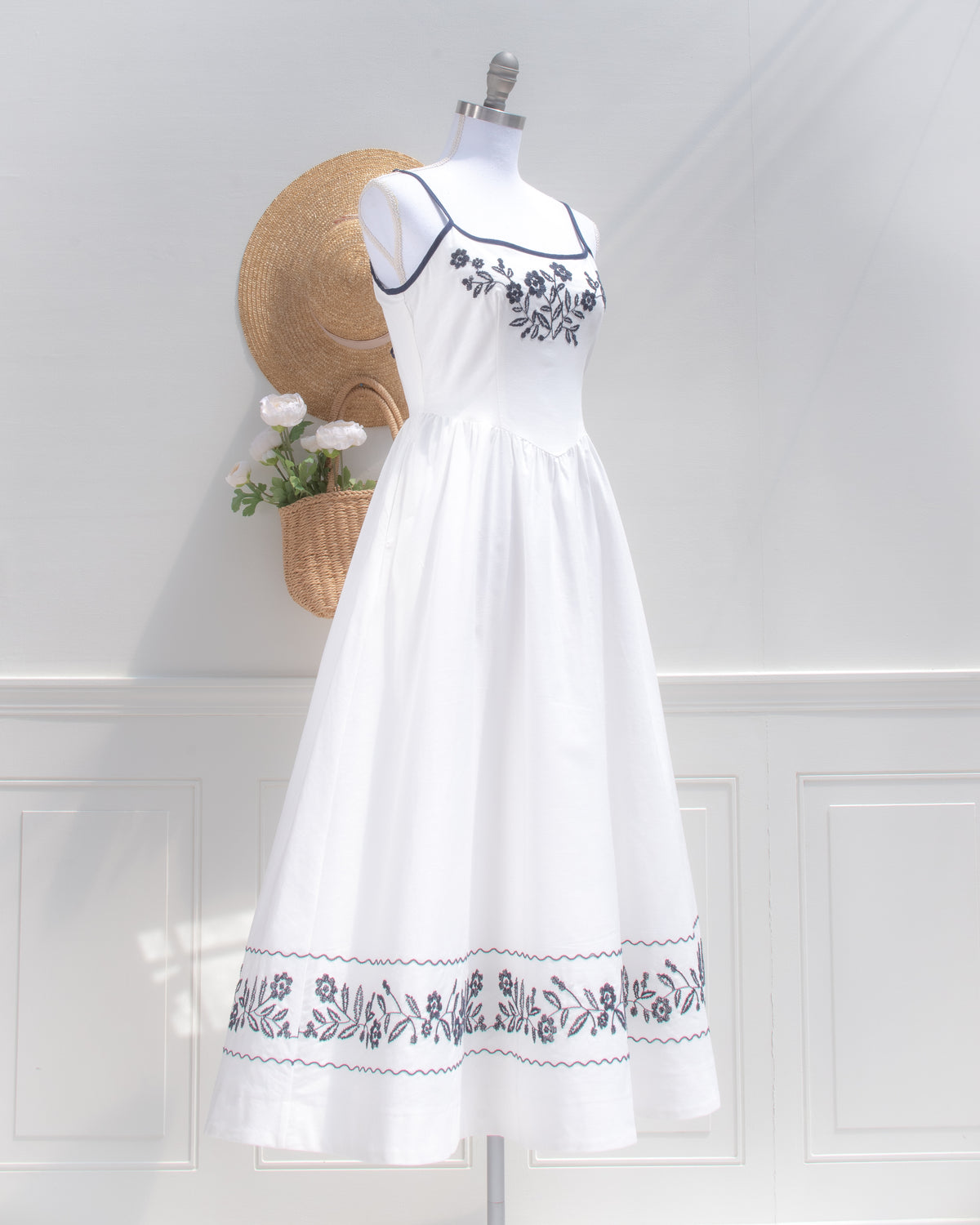 Three-quarter view of the white embroidered dress, with navy straps, a floral bodice and a full midi skirt.