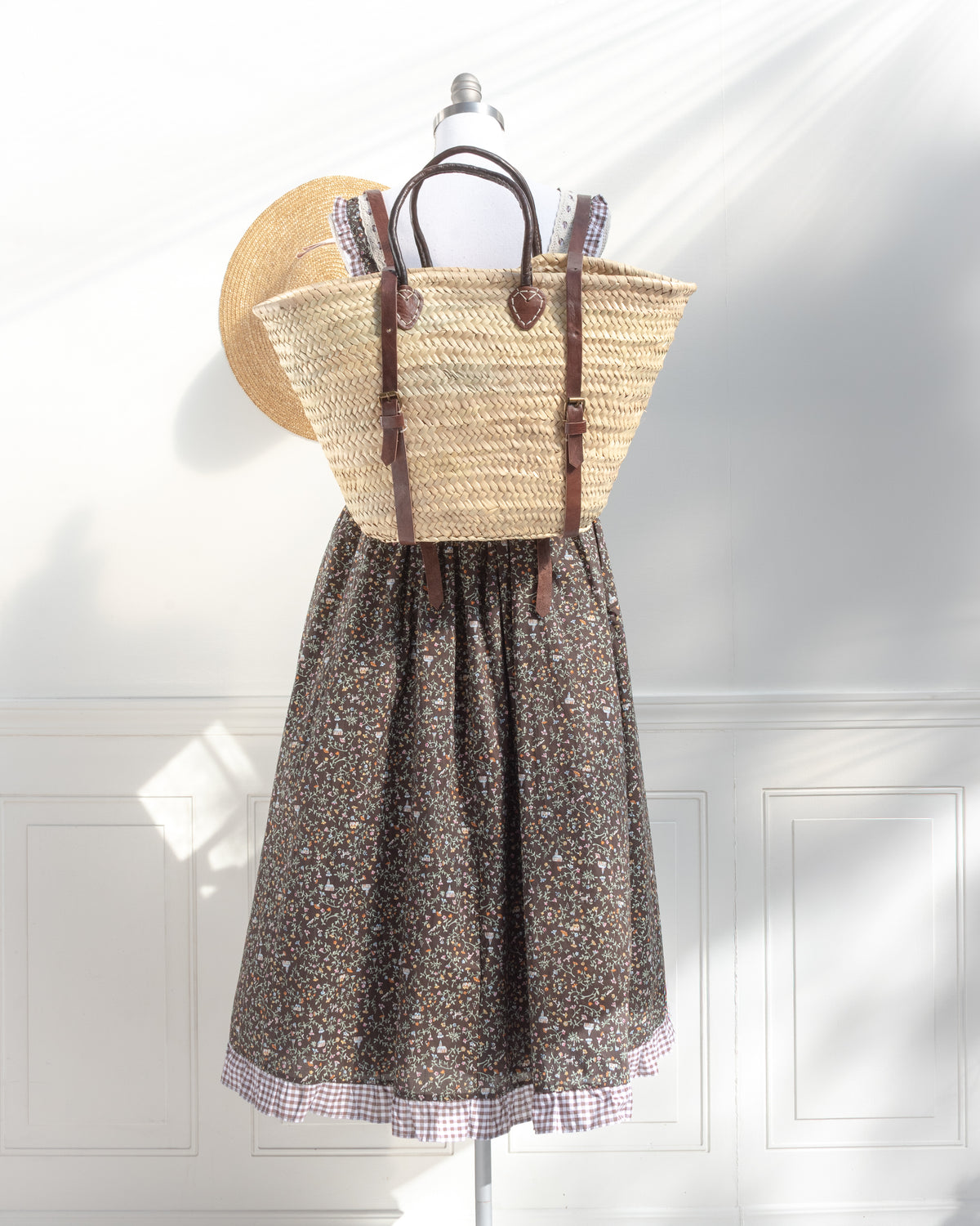French countryside look: the woven straw tote worn as a backpack over a brown floral dress with gingham hem.