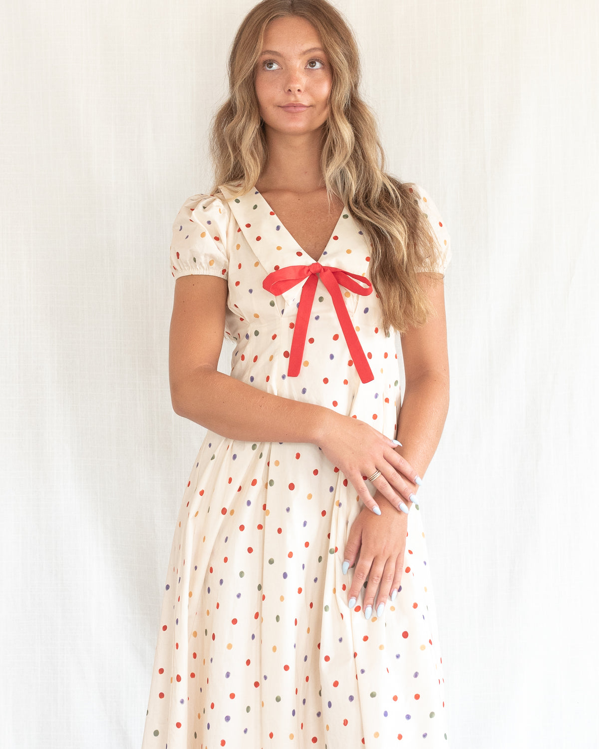 Close-up of the wide collar, coral bow and puff sleeves on the cream polka dot dress, worn by a model.