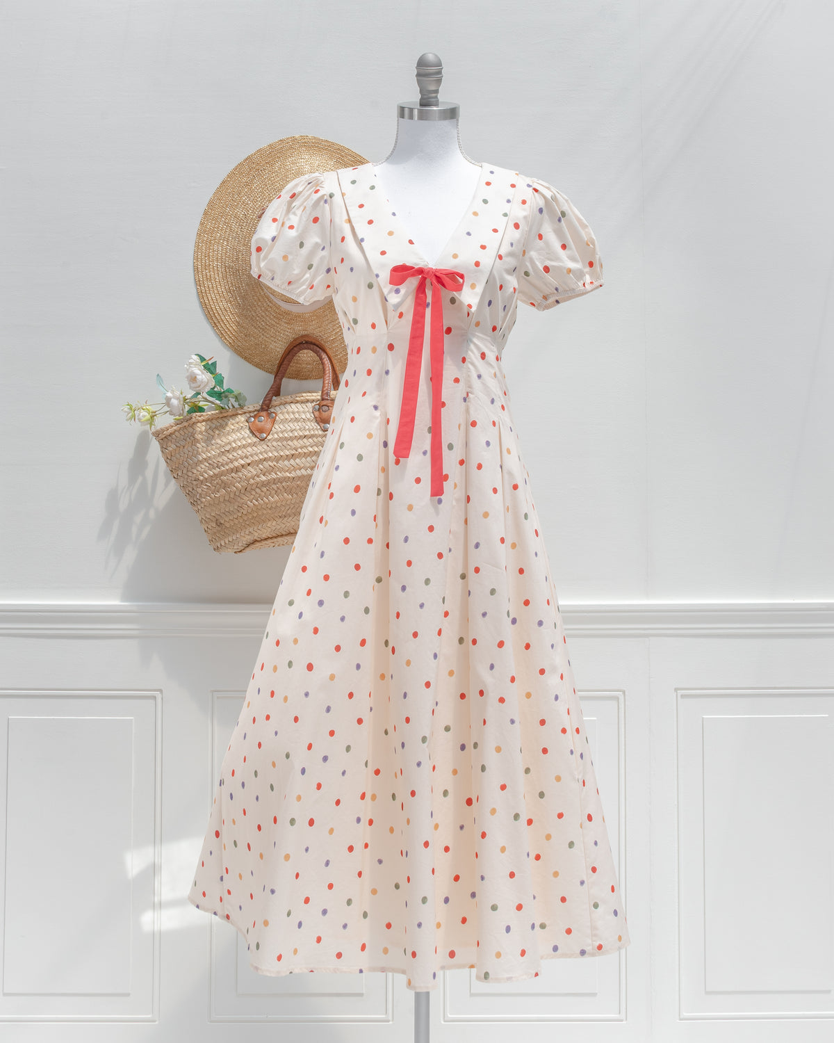Front view of the Margot dress, a vintage-inspired cream polka dot midi dress with a wide collar and coral bow.