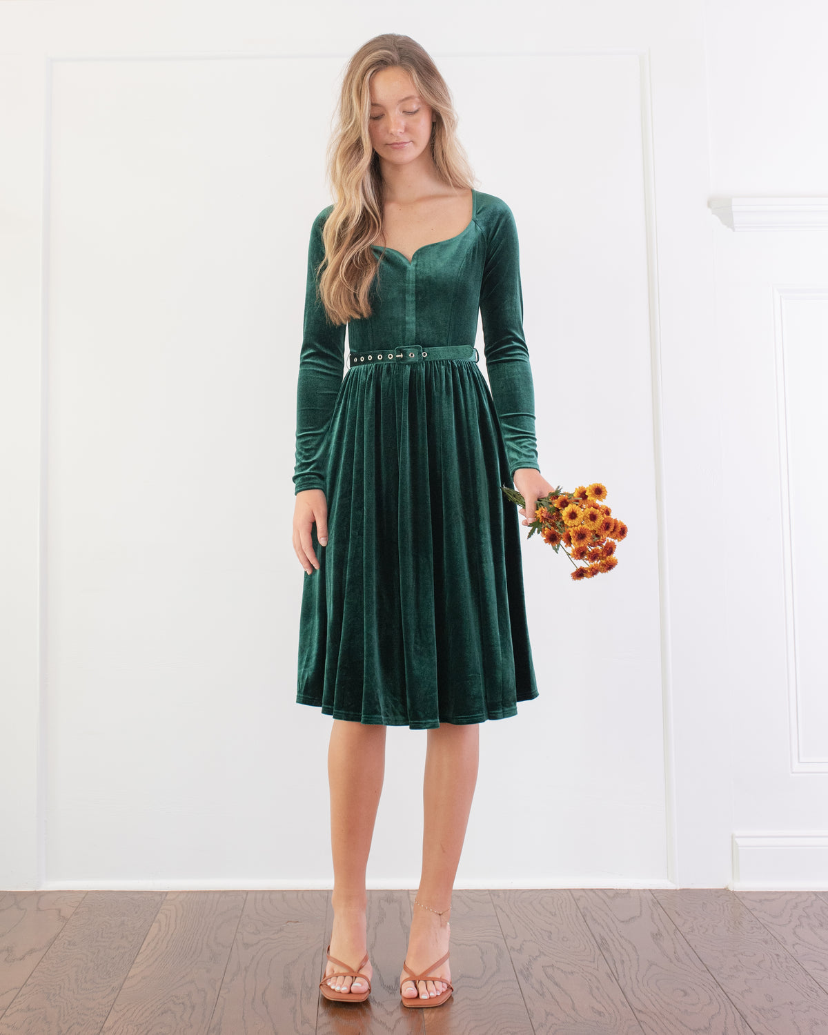 Worn by a model with tan strappy heels and a belt at the waist, the emerald velvet dress has a graceful sweetheart neckline.