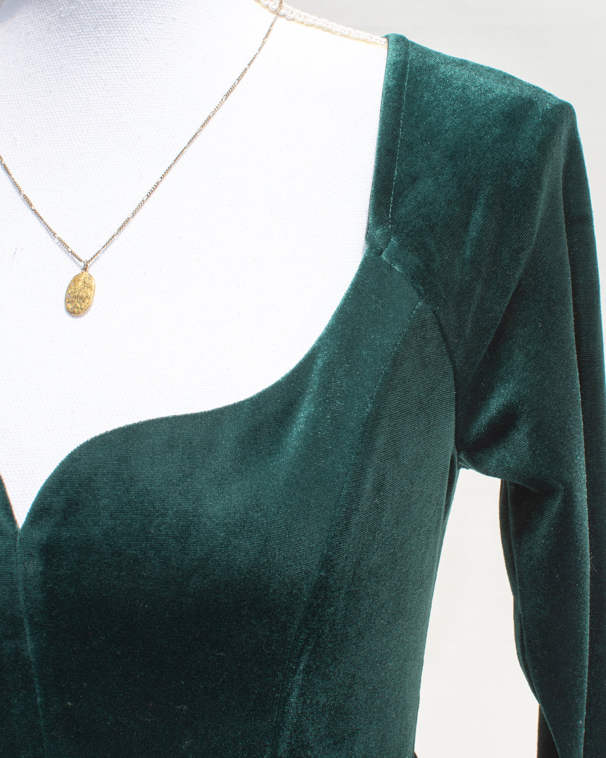 Close-up of the sweetheart neckline and long sleeve on the emerald velvet dress, shown on a dress form.