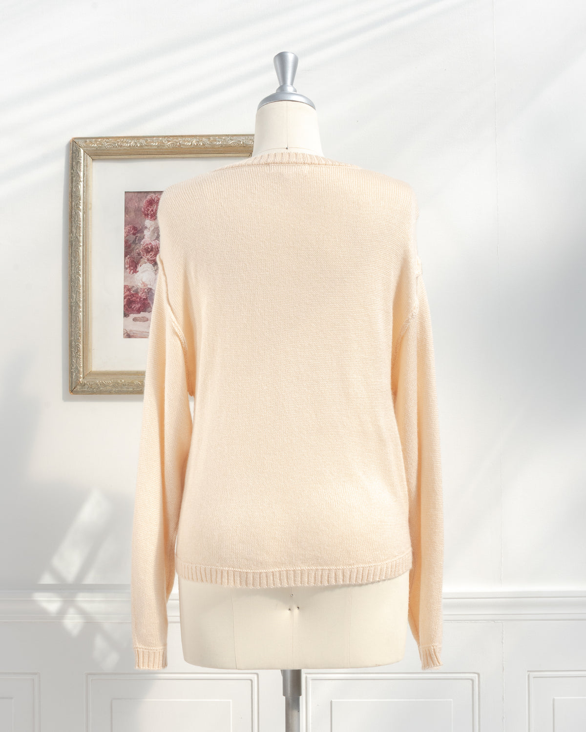 Beige knit sweater with ribbed hem and cuffs on a mannequin, back view.