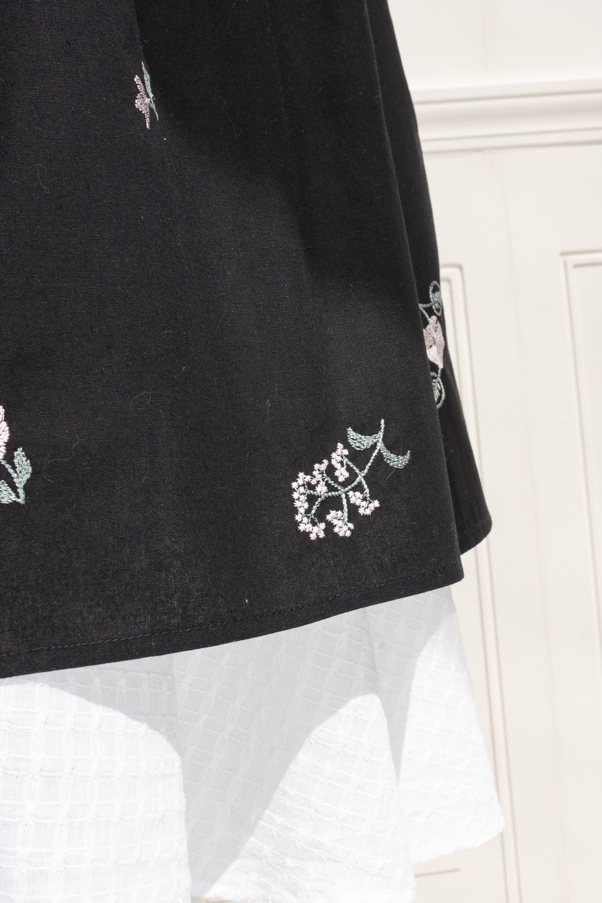 Close up of scattered botanical embroidery on black apron skirt.