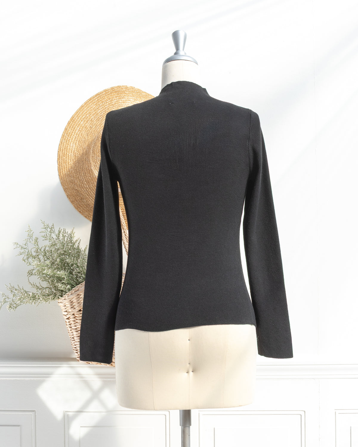 Black knit top with clean silhouette and long sleeves on a mannequin, back view.
