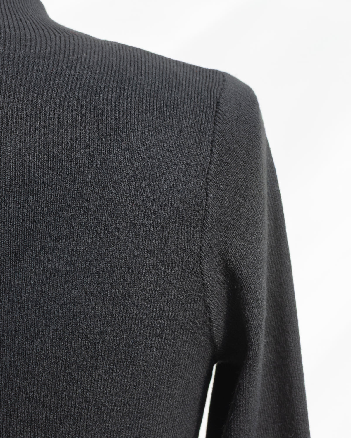 Black knit top with fine ribbed texture and shoulder seam, shoulder detail view.
