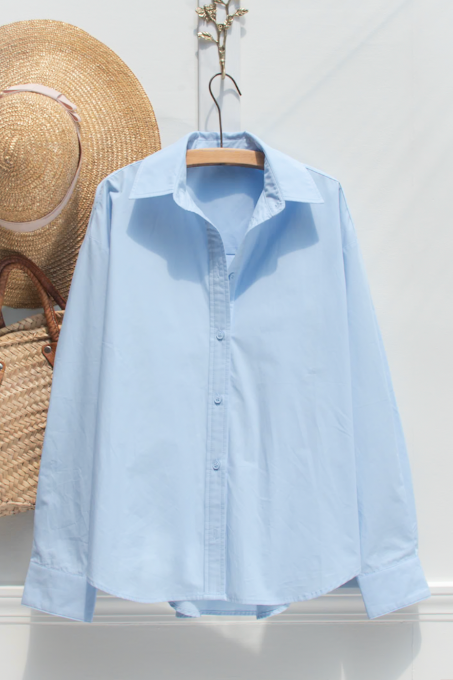 Blue cotton button up shirt shown on a hanger, front view.