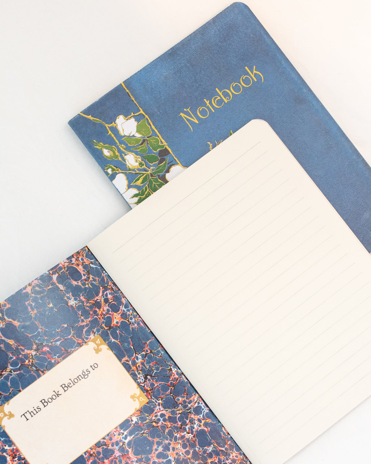 Open blue vintage notebook showing blue marbled endpaper, a name label, and a lined page, angled flat lay view.