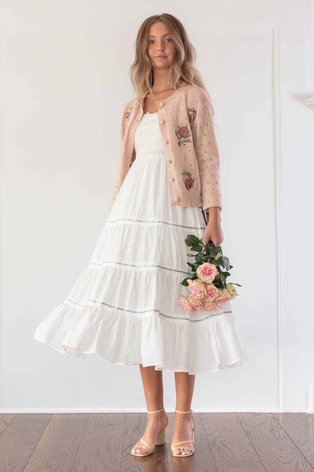Blush pink cardigan with rose embroidery worn open, model styled holding a bouquet of roses.