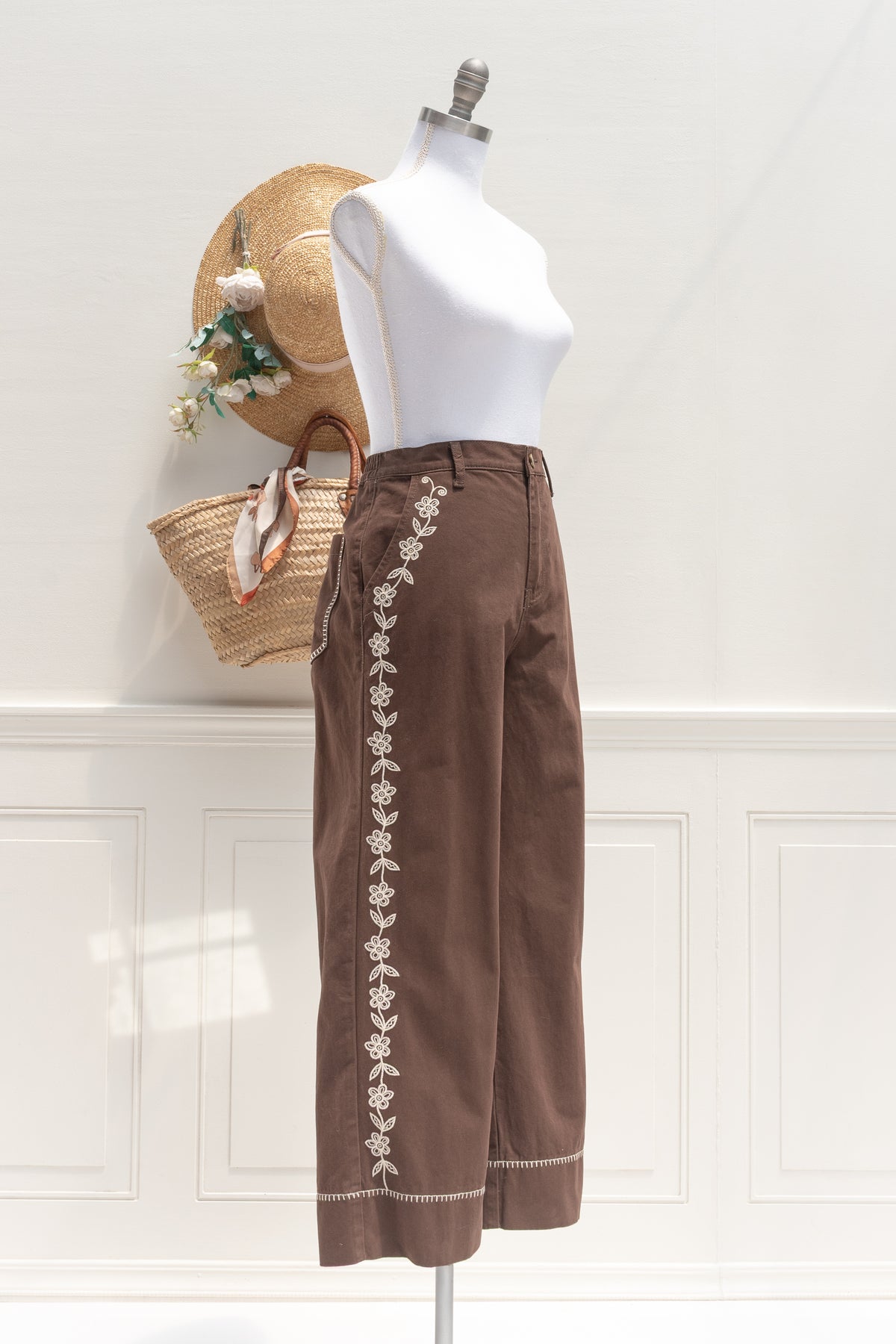 Brown cotton denim pants with floral embroidery, a timeless silhouette shown on a mannequin, three quarter view.