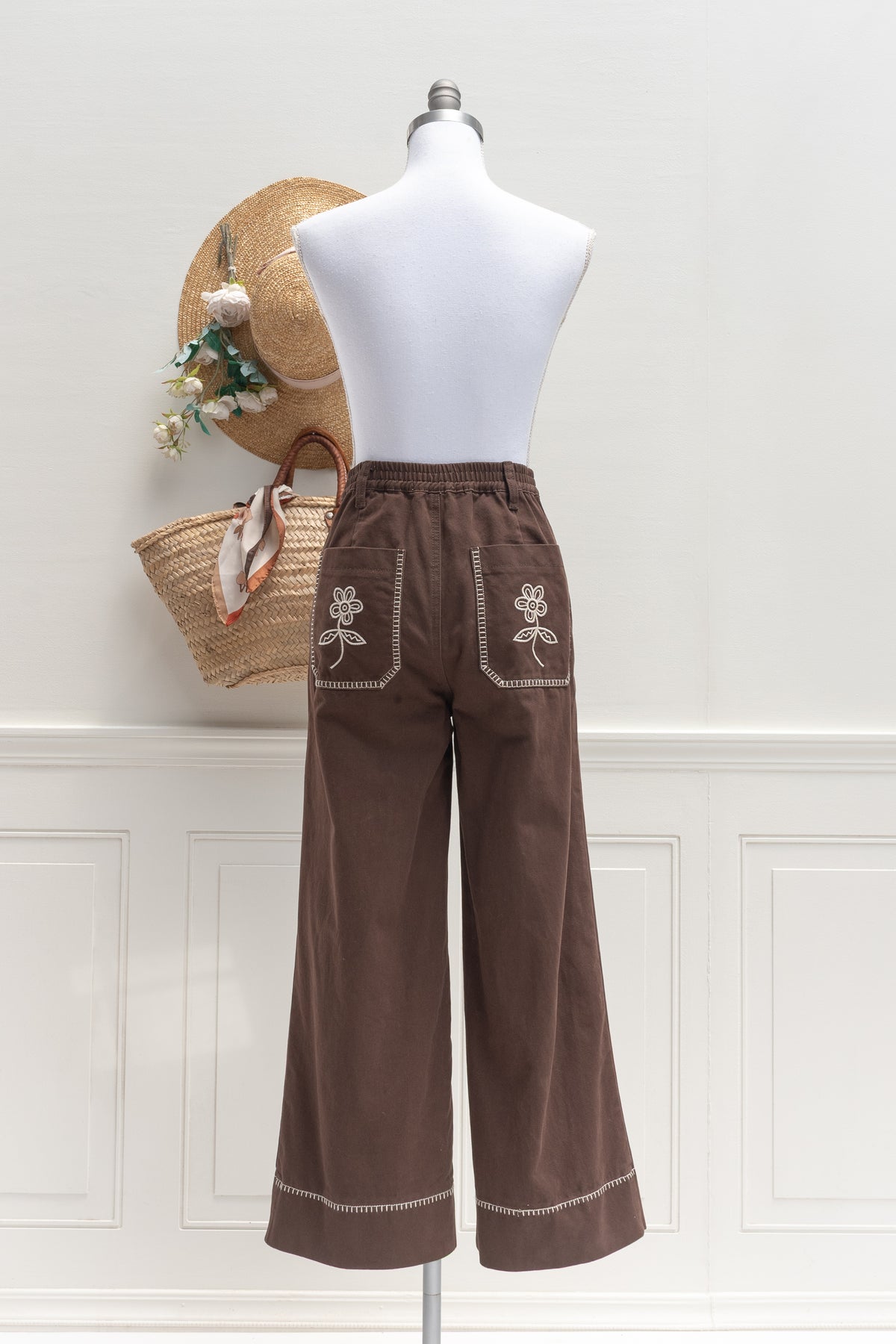 Brown cotton denim pants with embroidered back pockets, a feminine silhouette shown on a mannequin, back view.