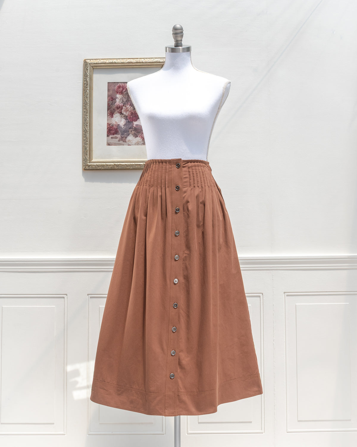 Brown cotton midi skirt with pleated waist and button front, mannequin front view.