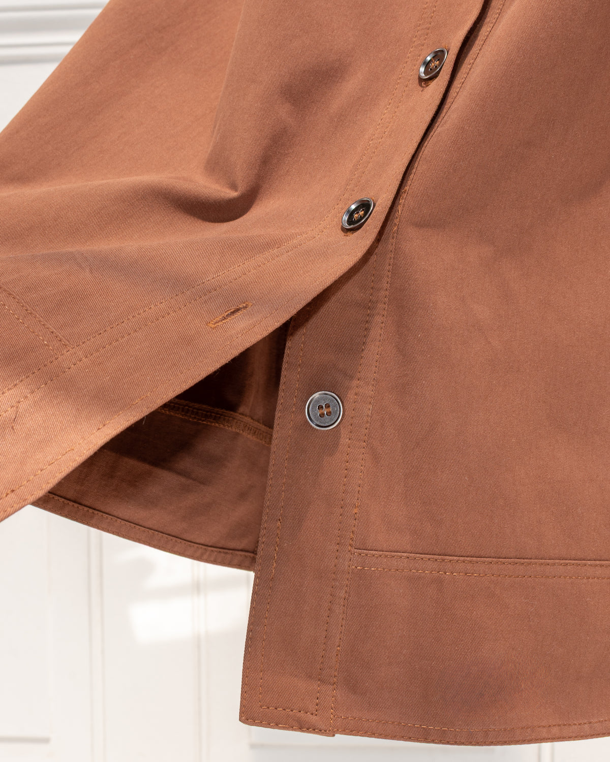 Brown cotton midi skirt with button placket and topstitched hem, close detail view.