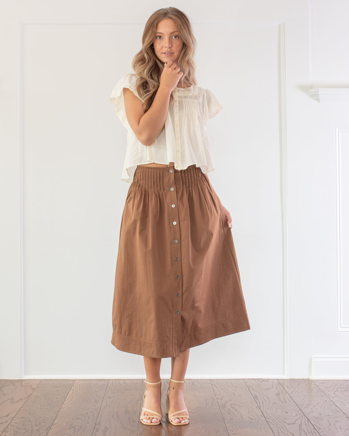 Brown cotton midi skirt styled with a cream blouse, a classic wardrobe staple, model front view.