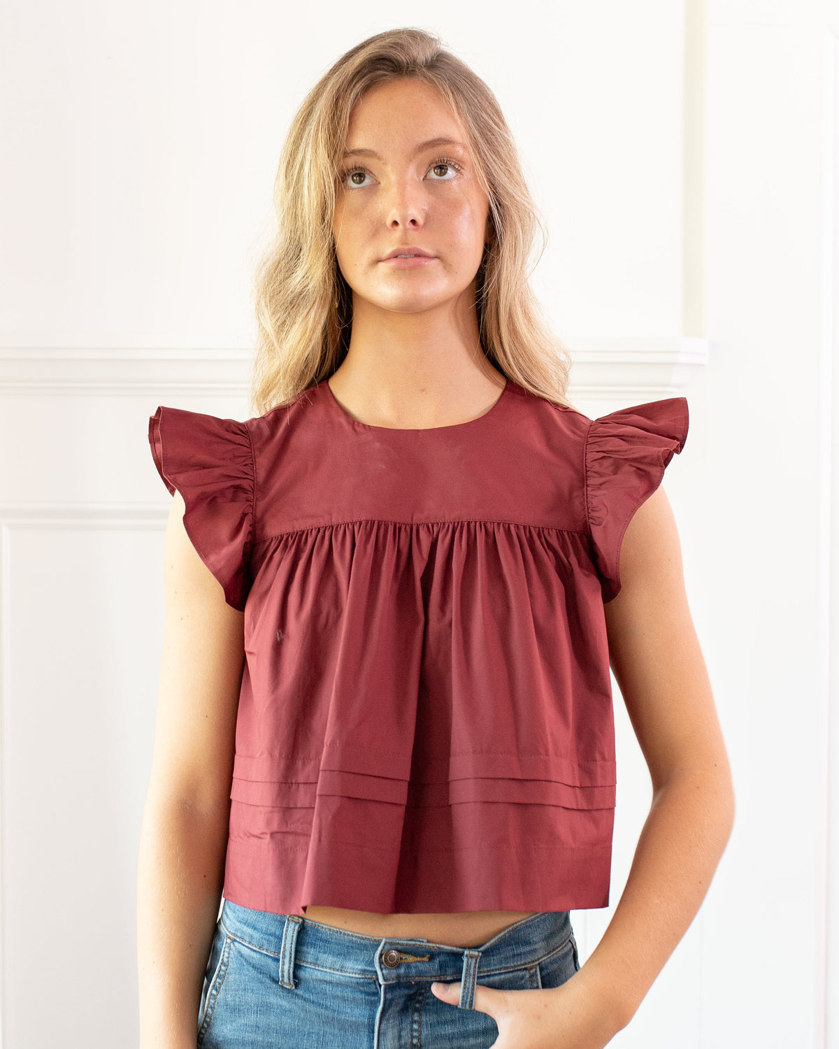Burgundy cotton flutter sleeve top with a rounded neckline, worn with jeans, French girl style, front view.