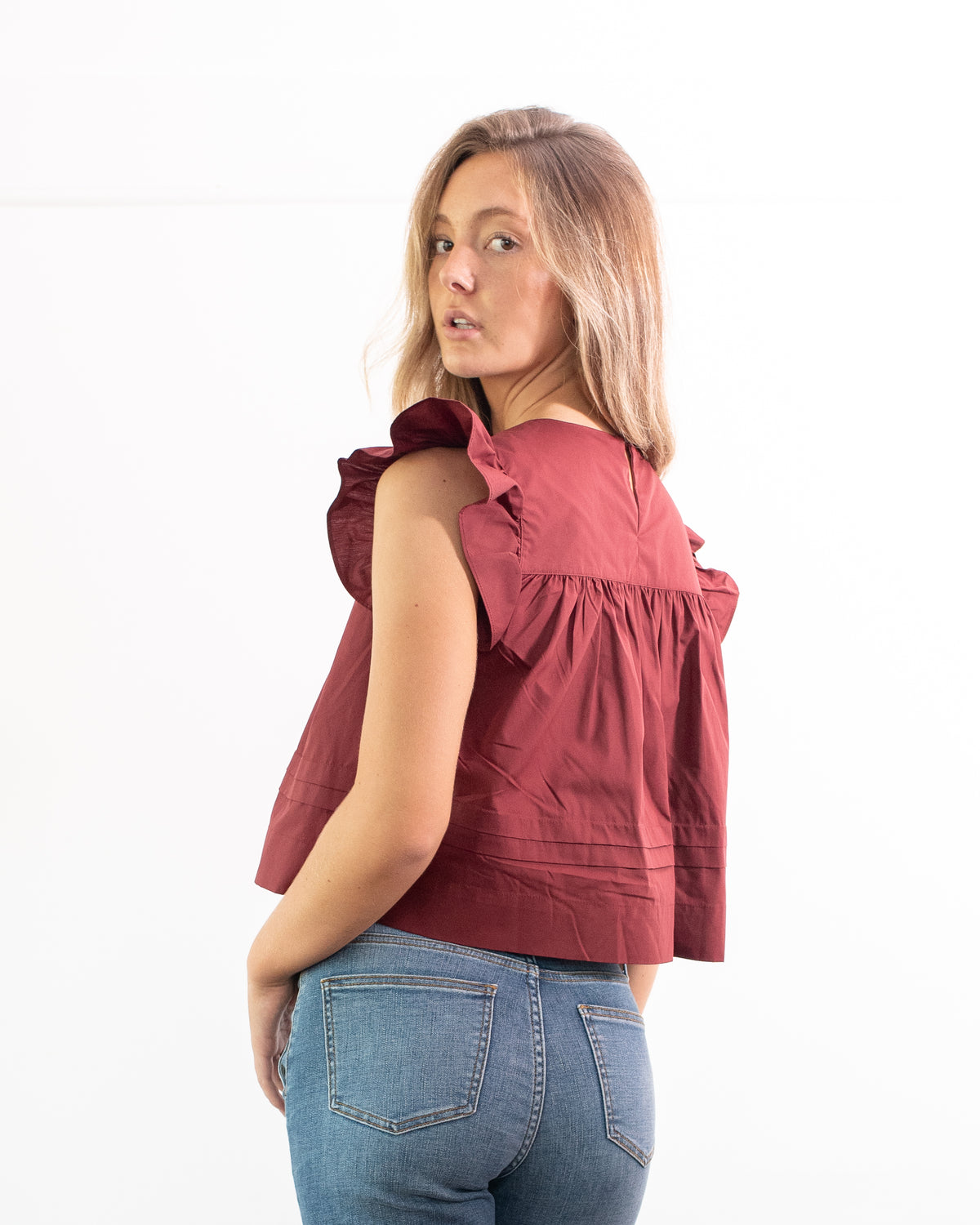 Burgundy cotton flutter sleeve top with a keyhole back, worn with jeans, French girl style, back three quarter view.