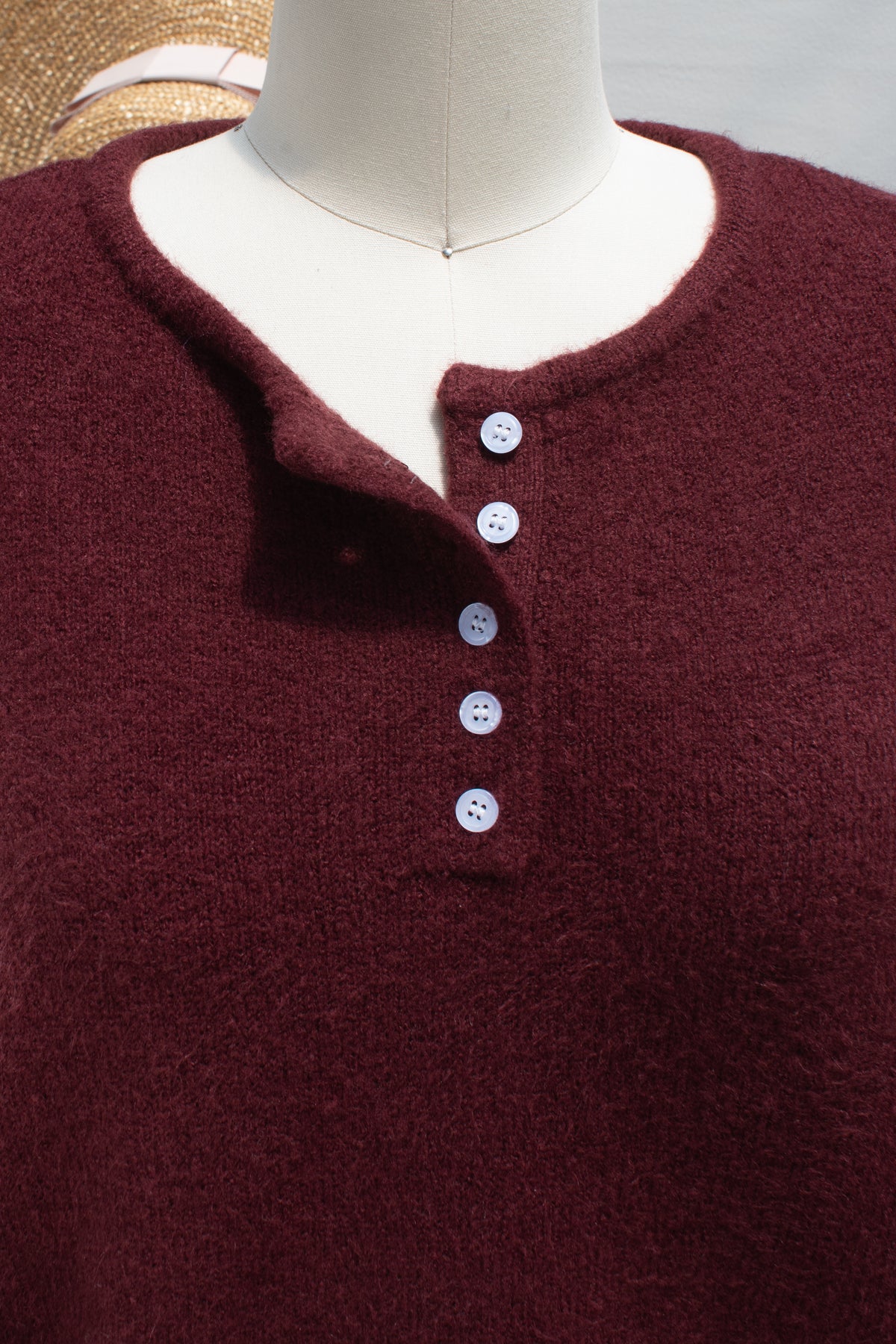 Close up of the button placket and henley neckline on a burgundy knit sweater.