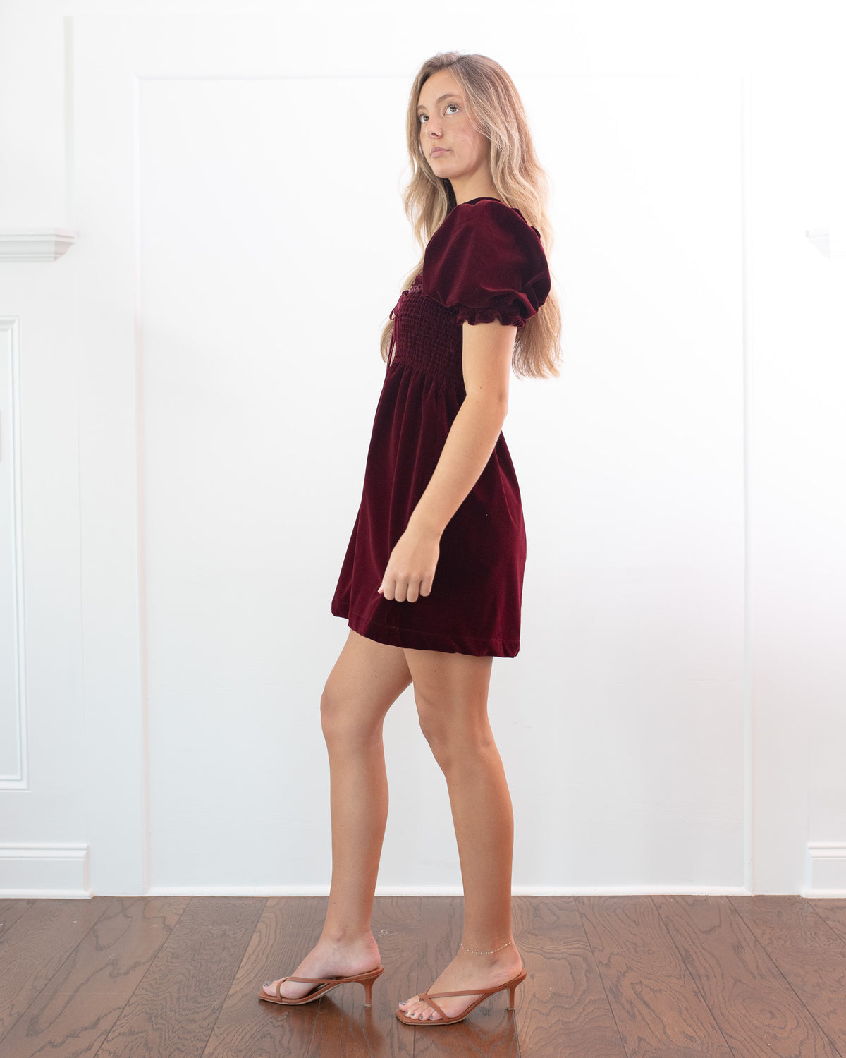 Burgundy velvet babydoll mini dress with a smocked bodice and puff sleeves, full length side view.