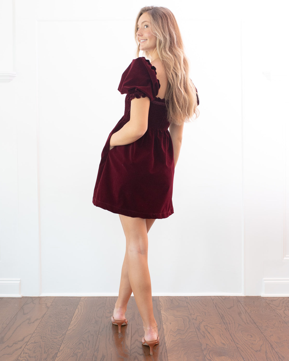 Burgundy velvet mini dress with puff sleeves and a side pocket, feminine vintage inspired, back three quarter view.