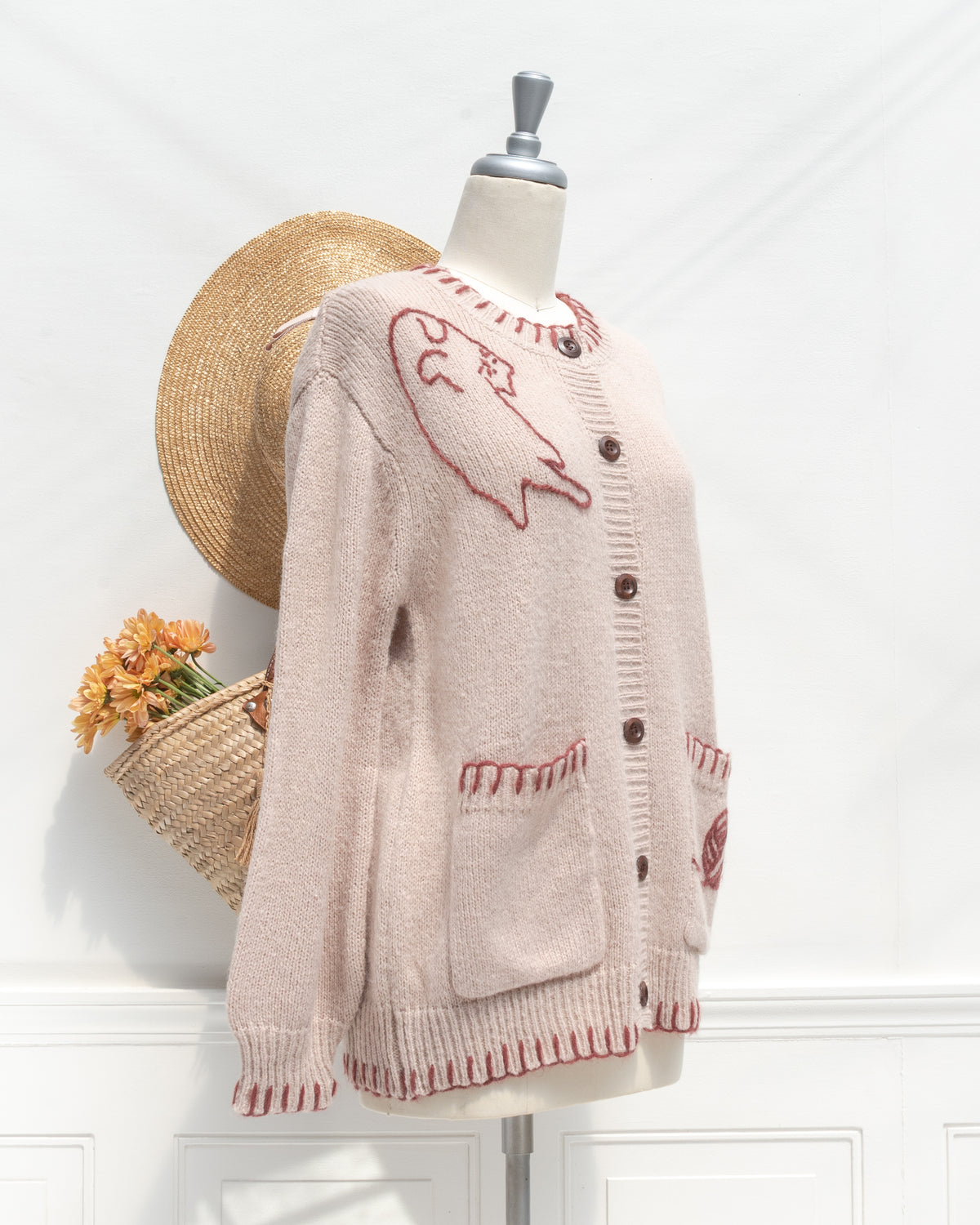 Blush knit cardigan with shoulder cat embroidery and patch pockets, mannequin three quarter view.