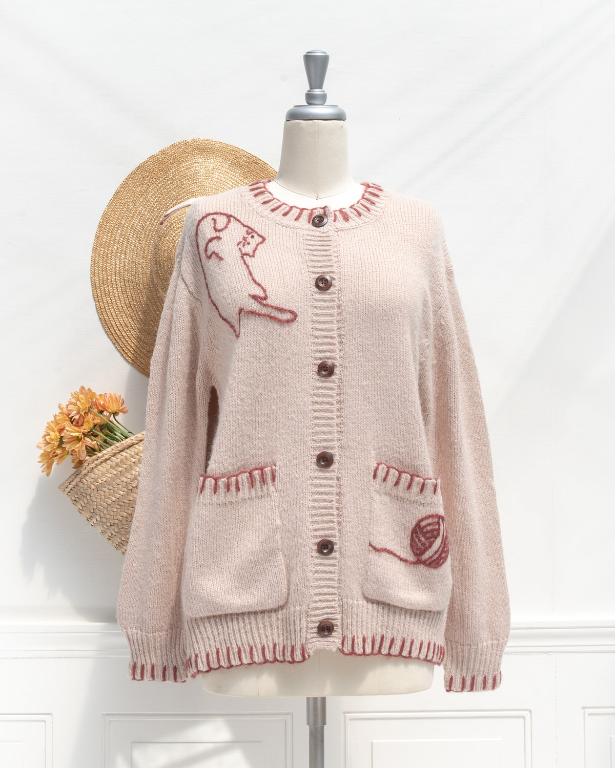 Blush knit cardigan with cat embroidery and a yarn ball pocket, a classic wardrobe staple, mannequin front view.