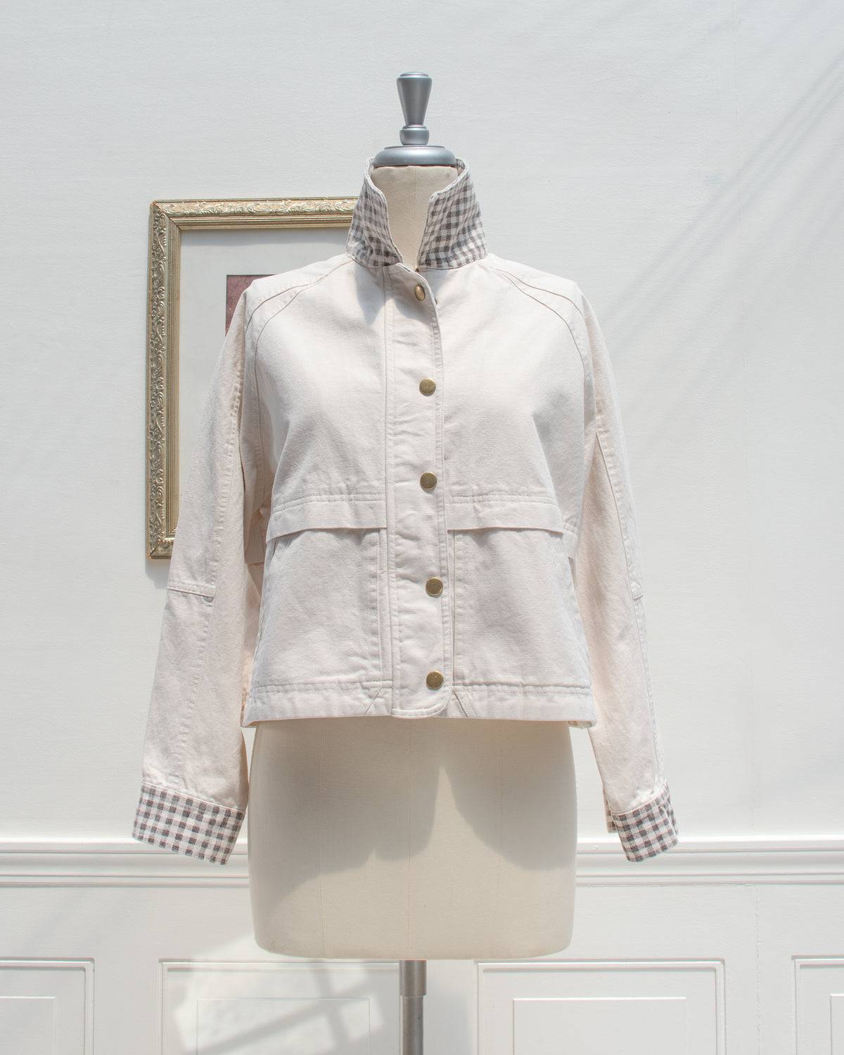 Front view of the Marlowe Jacket snapped closed, a feminine style cream cotton chore jacket with a gingham stand collar and gingham cuffs.