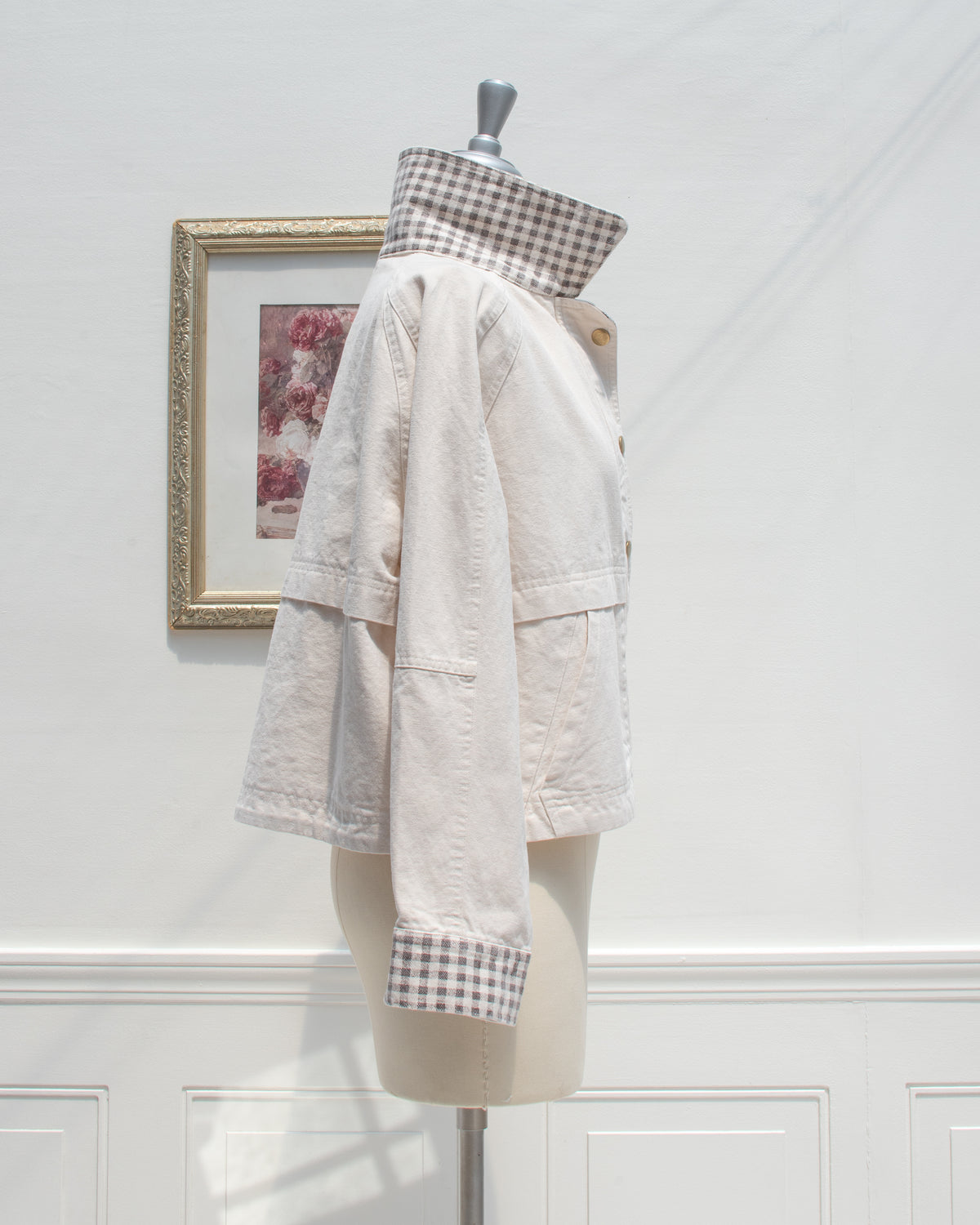 Side profile of the Marlowe Jacket, a cropped cream cotton chore jacket with a raised gingham collar, raglan sleeve, and gingham cuff.