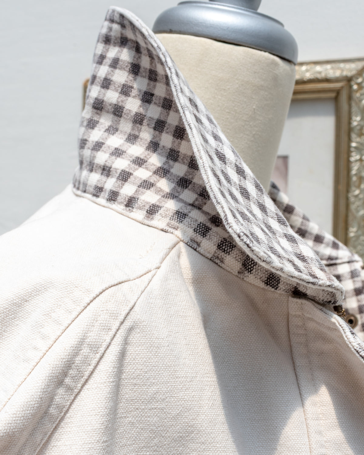 Detail of the Marlowe Jacket gingham collar turned up, showing the raglan shoulder seam and the texture of the cream cotton canvas.
