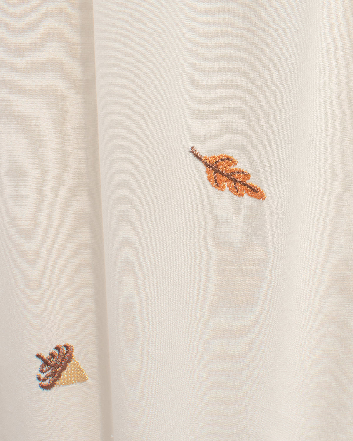 Close up of rust orange leaf and brown acorn embroidery on cream cotton, a romantic detail of a feminine French inspired fall dress. 