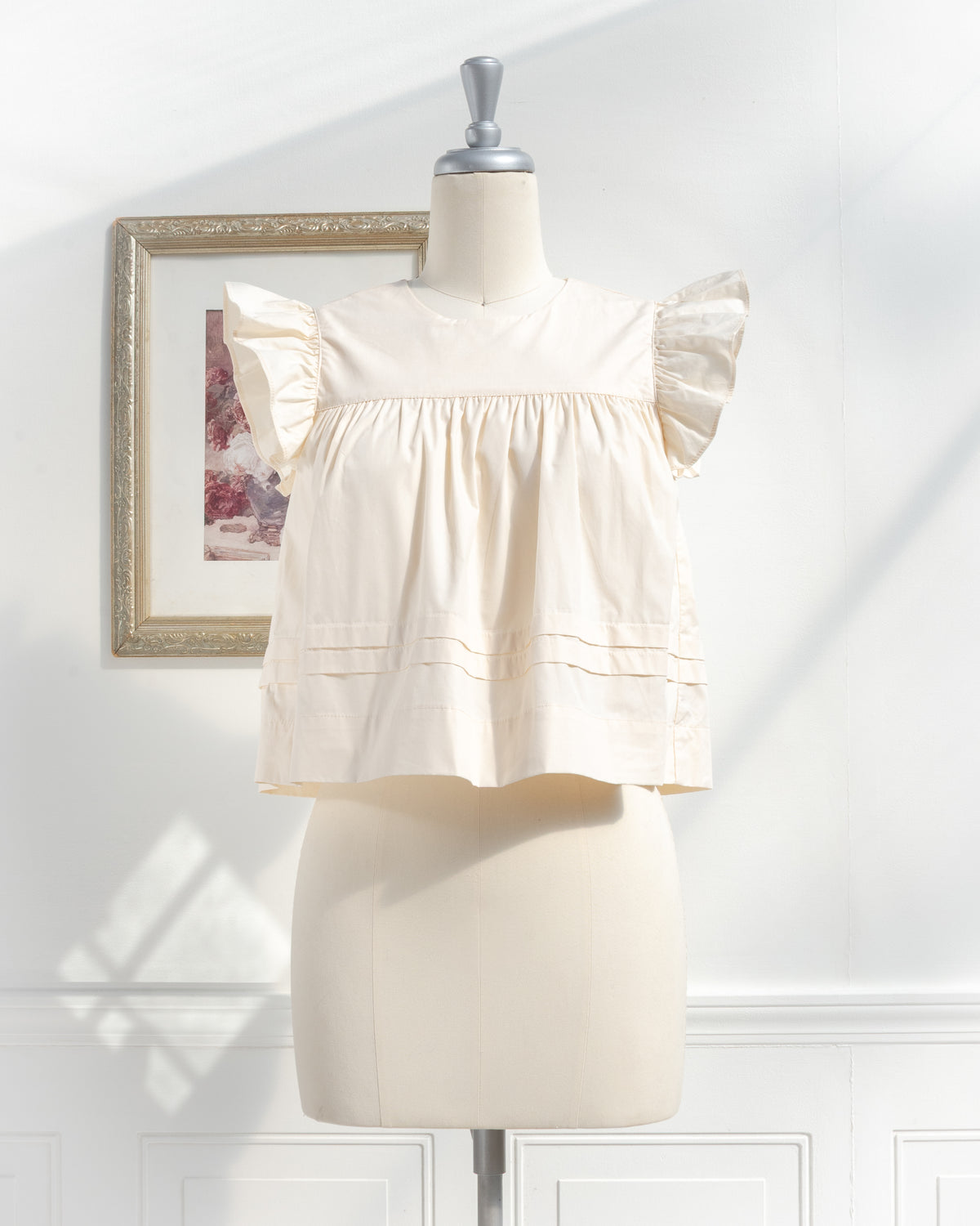 Cream cotton flutter sleeve top with pintuck hem styled with jeans and a straw basket, French girl style, front view.