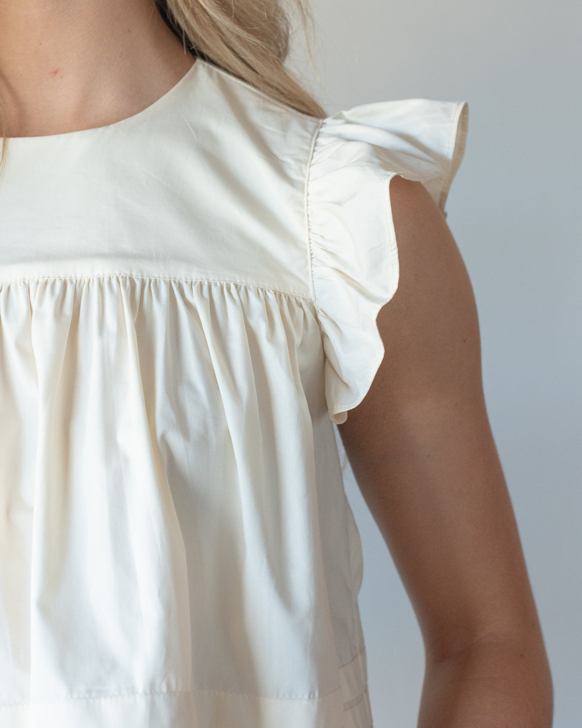 Cream cotton flutter sleeve top with a gathered yoke and rounded neckline, shoulder detail view.
