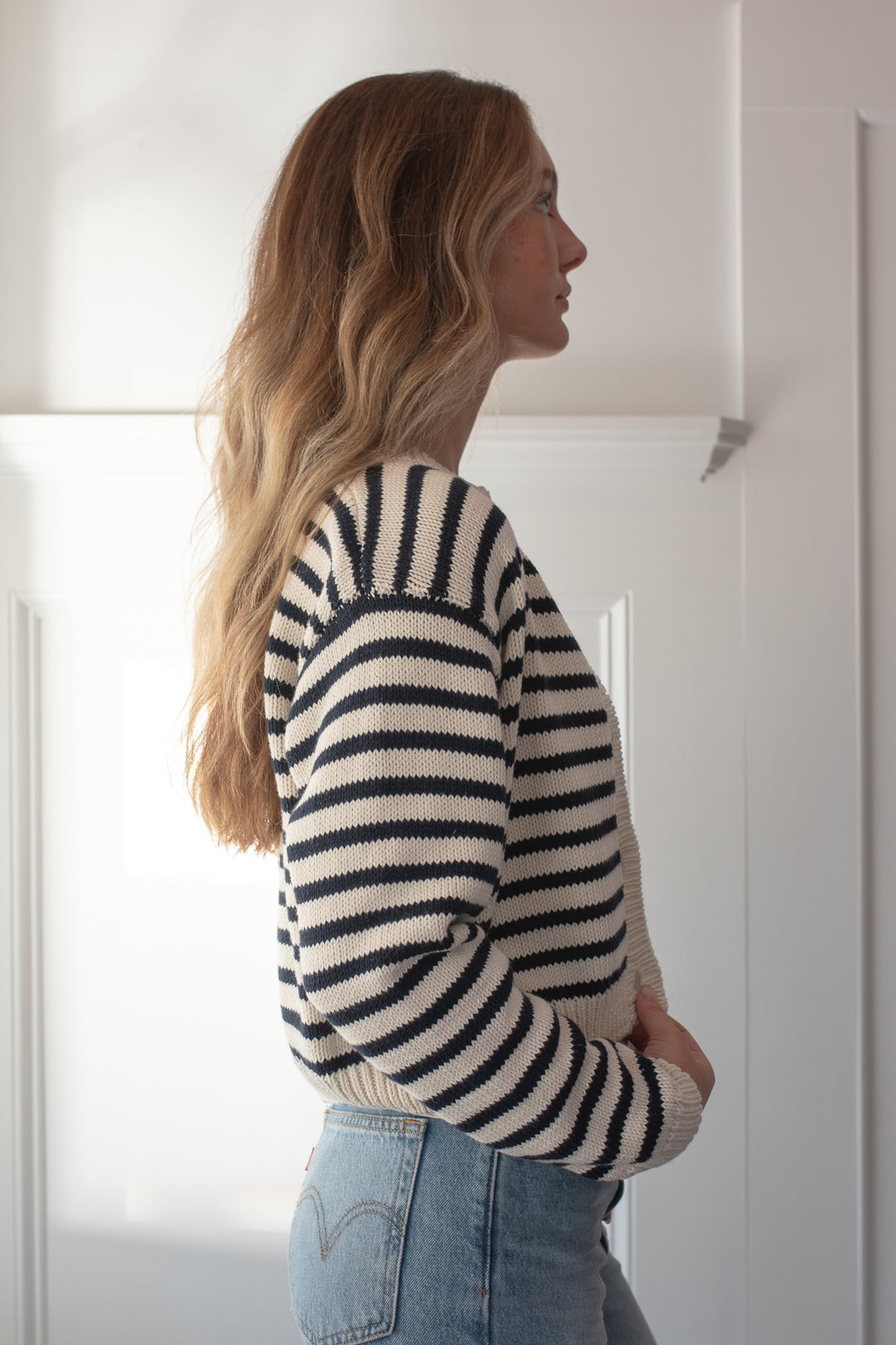 Cream and navy striped cotton cardigan with a button front on a model, side view.