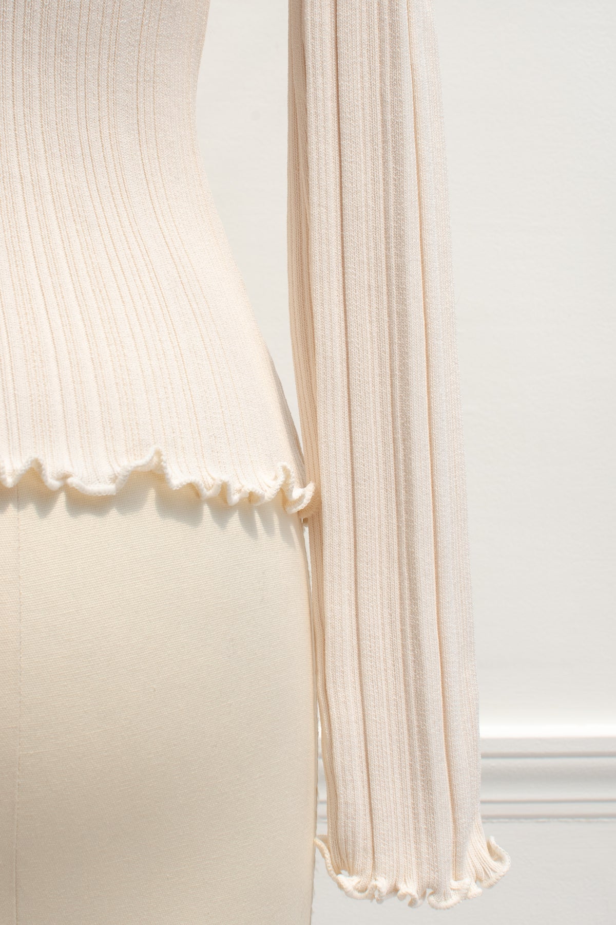 Detail of the lettuce-edge cuff and hem on the cream ribbed knit top.