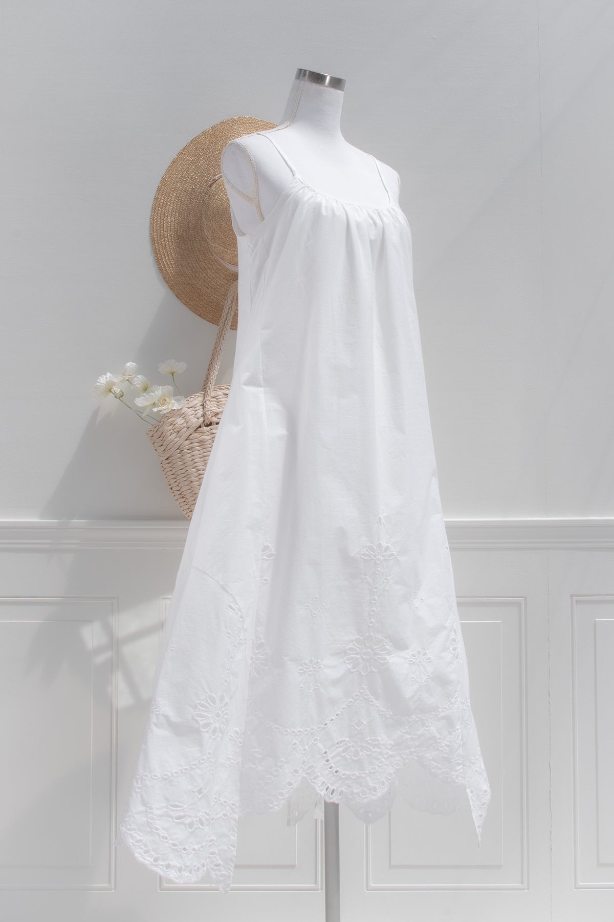 White cotton eyelet midi dress with cutwork hem and flowing silhouette three quarter view.