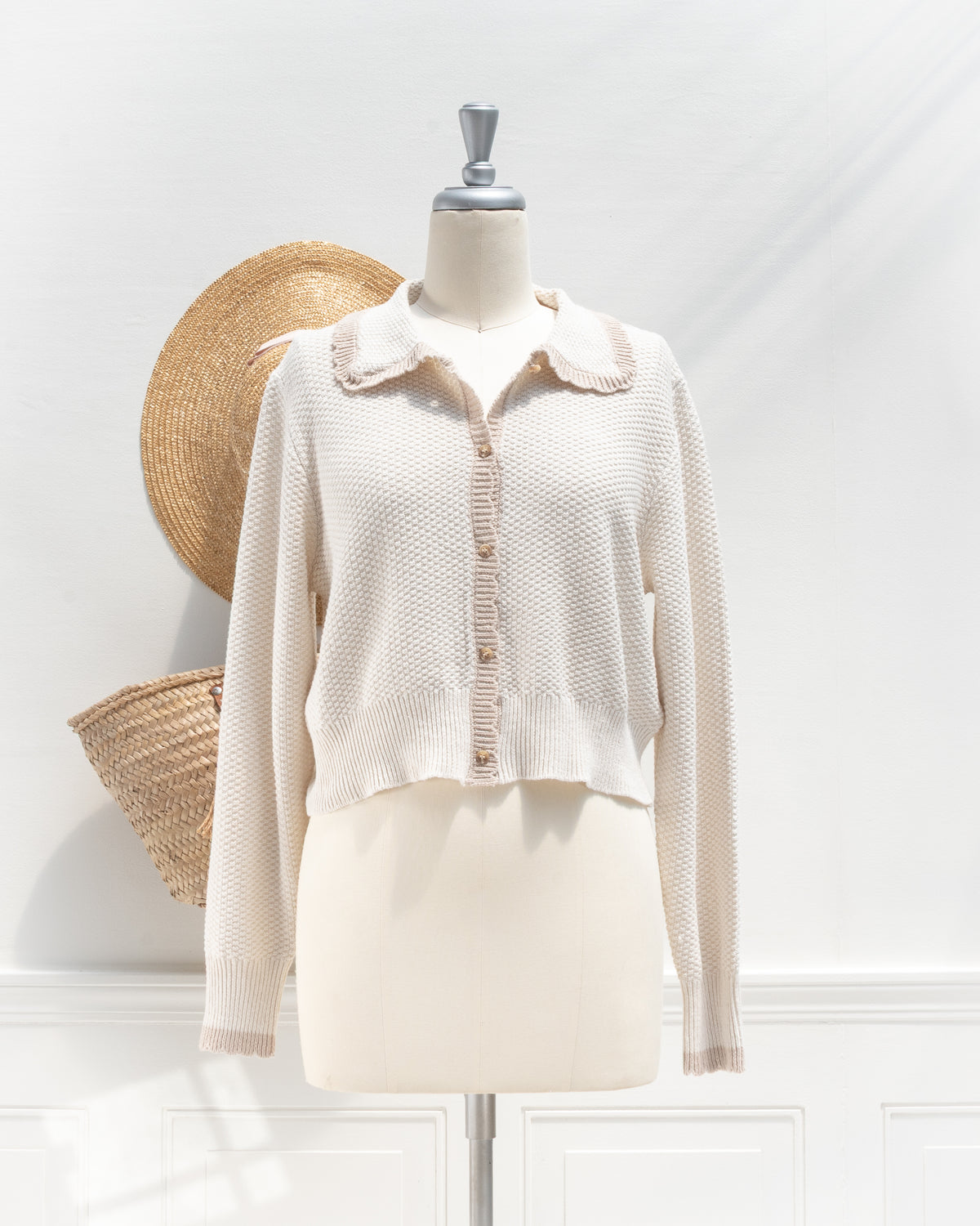 Ivory knit cardigan with tan scalloped collar and button placket, mannequin front view.