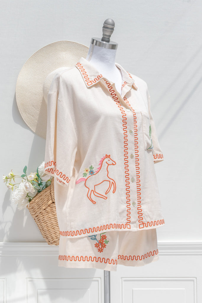 feminine clothing - a very unique summer set featuring a short sleeve button down shirt and shorts. In cream linen blend, it features very cute embroidery including a horse, and florals. A beautiful choice for your summer getaways. 3/4 side view. amantine french style clothing. 