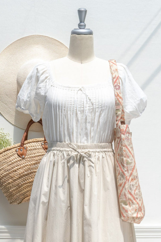 Mannequin wearing a white top and beige skirt with a straw bag and hat on a white background