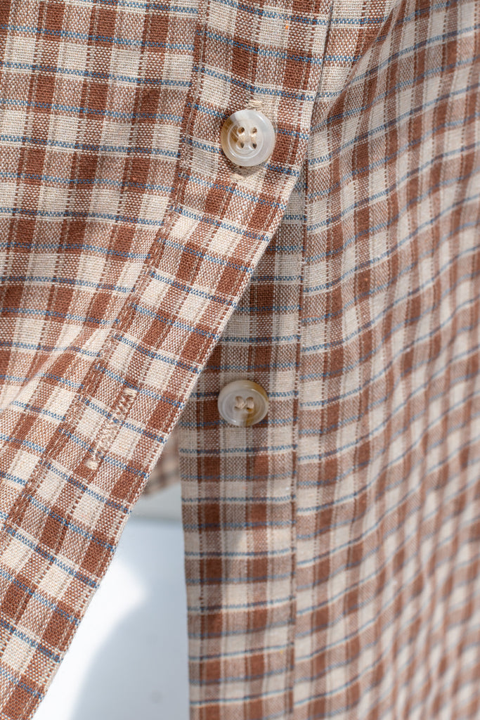 Close-up of a brown and beige plaid shirt with buttons on a white background