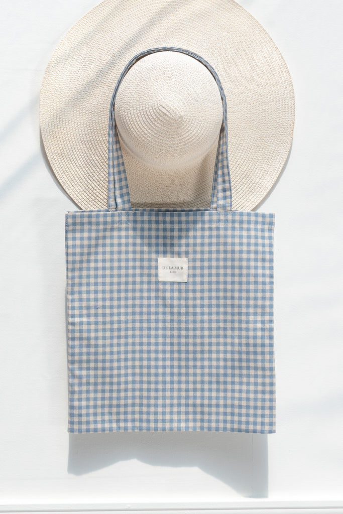 Blue gingham tote bag with a straw hat on a white background