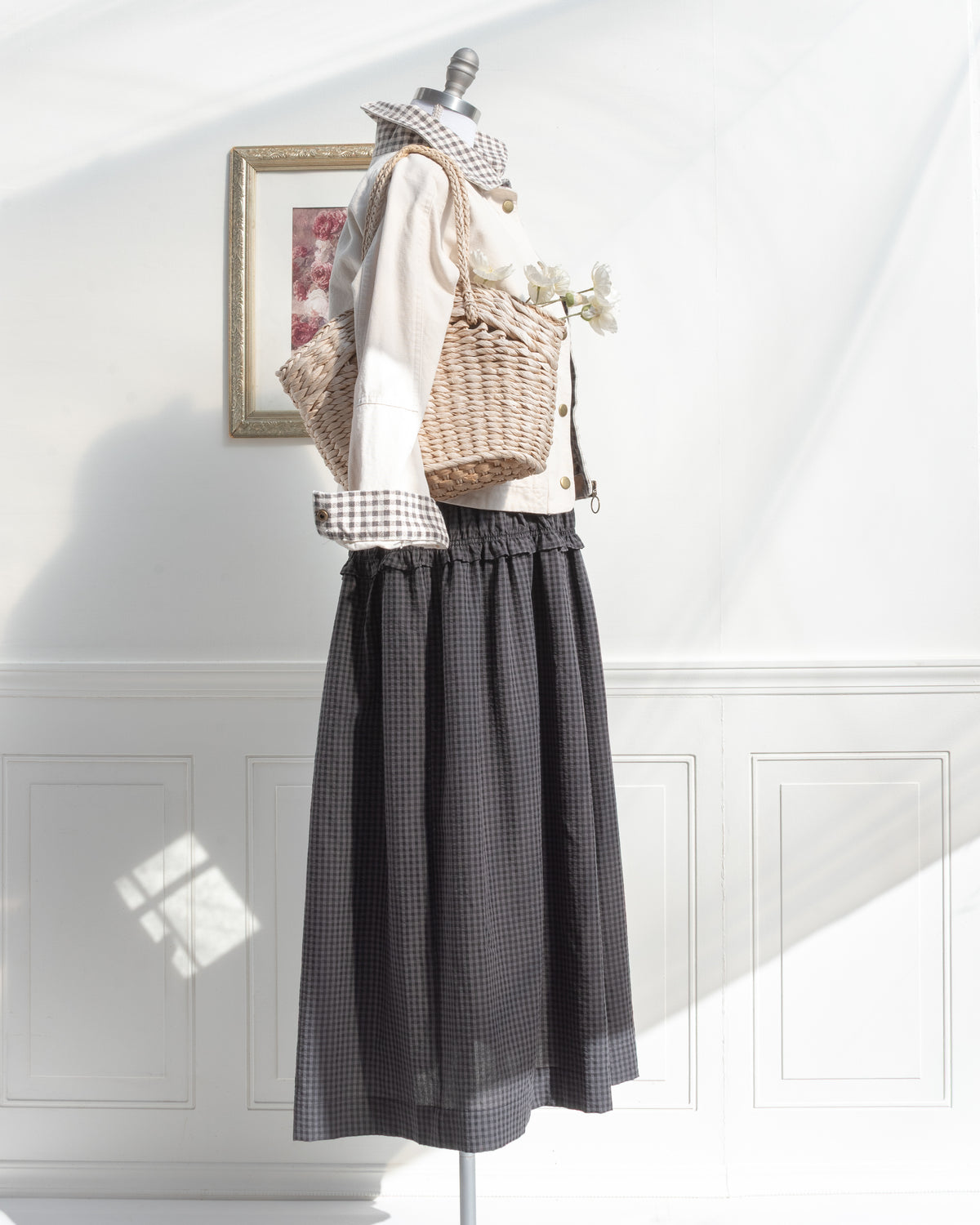 Gray plaid midi dress styled with a cream jacket and woven basket on a mannequin, feminine French girl style, side view.