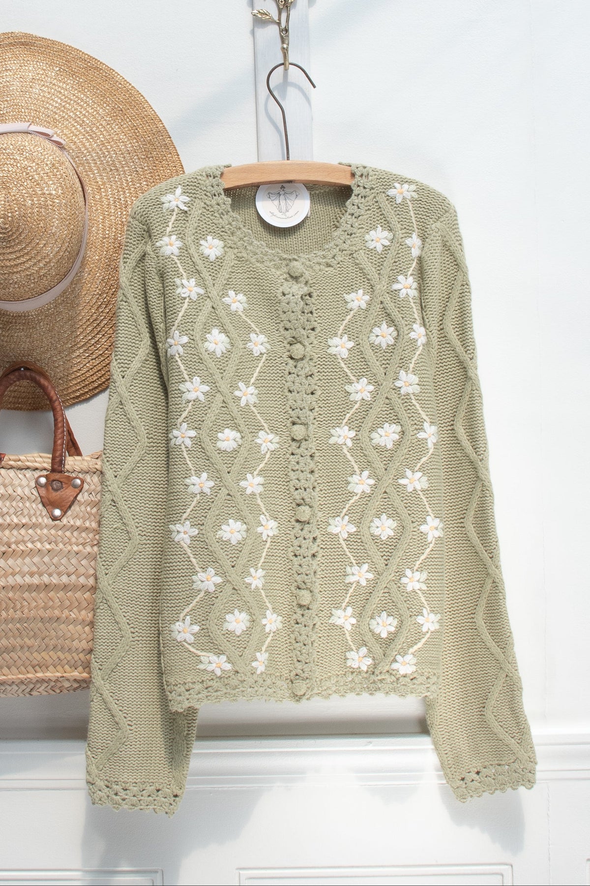 Green knit cardigan with white floral embroidery shown on a hanger, front view.