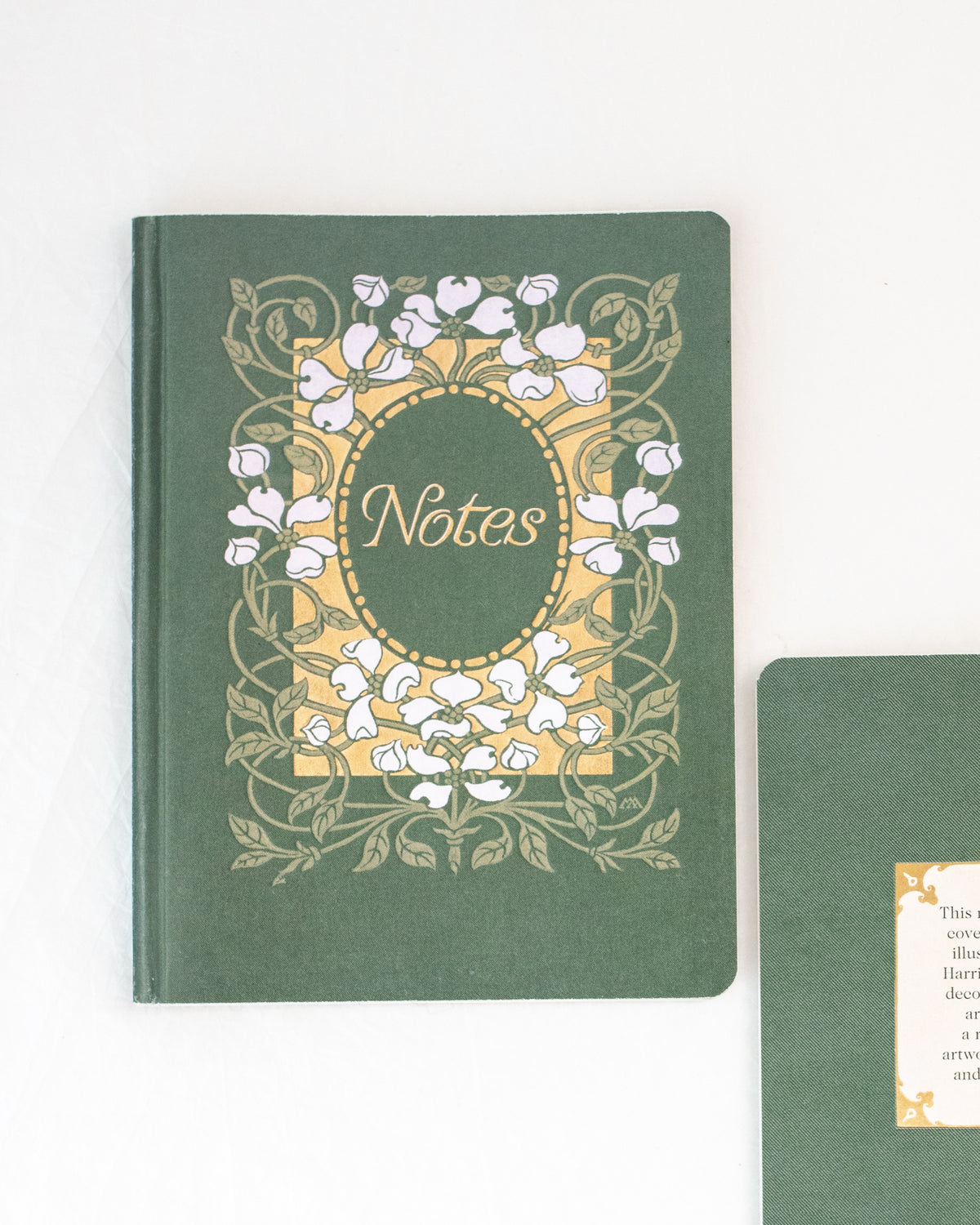 Green vintage notebook with white dogwood blossoms on a gold panel beside a back cover, overhead flat lay view.