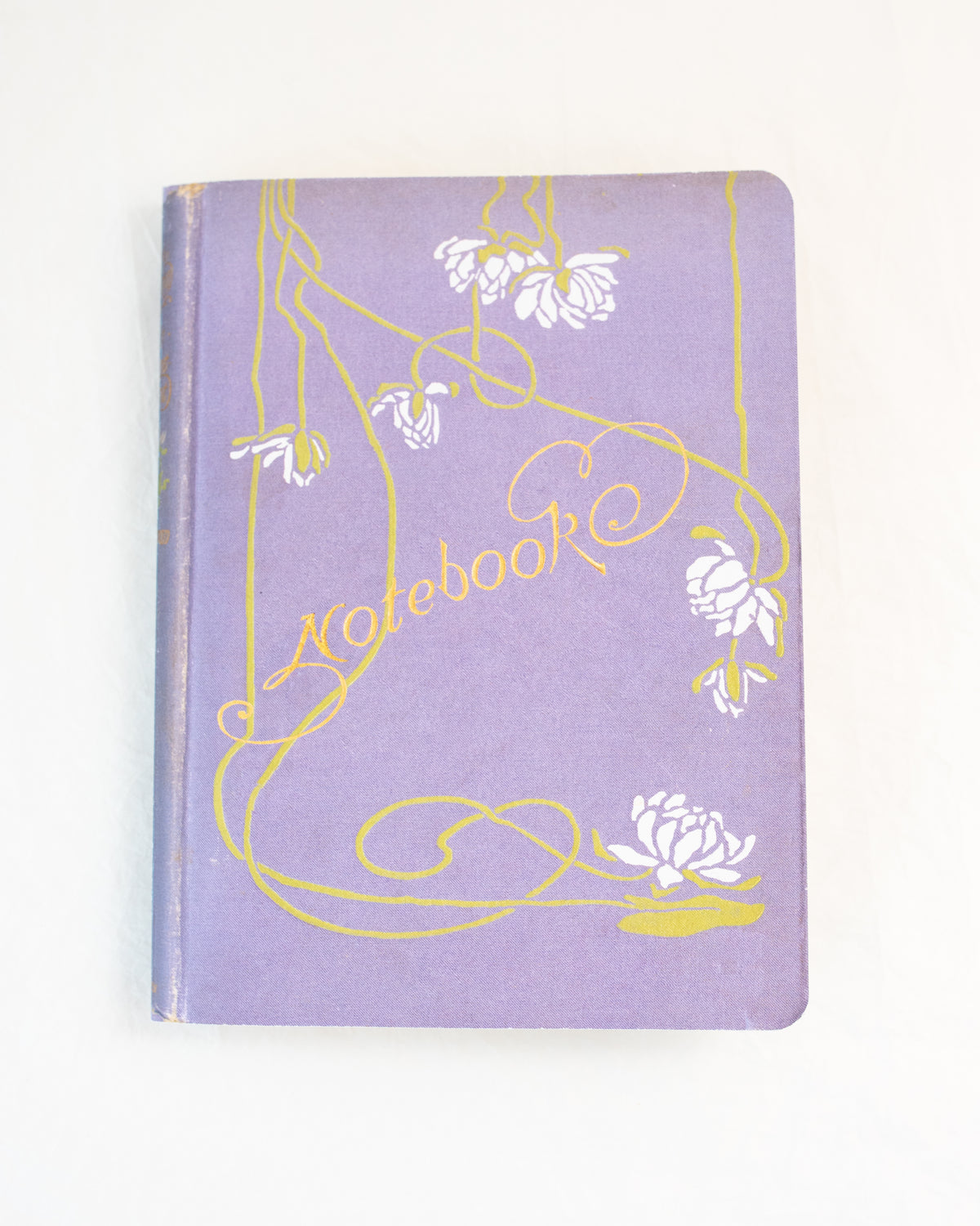 Lavender vintage notebook with white blossoms and green vines on the cover, flat lay overhead view.
