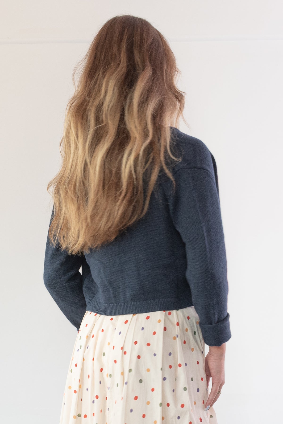 Navy cotton wool cropped cardigan worn over a polka dot skirt, model styled back view.