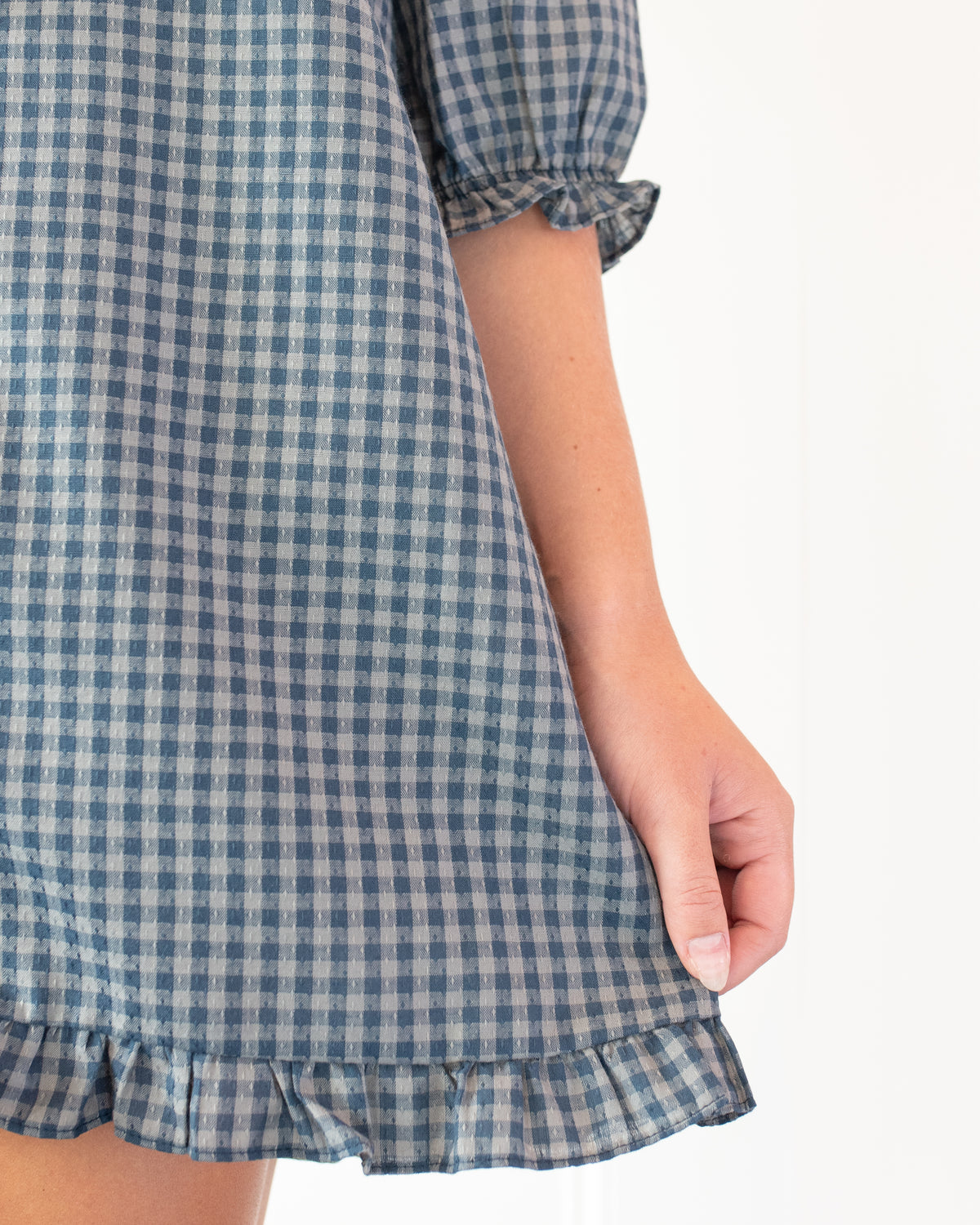 Navy gingham mini dress with ruffle hem and gathered sleeve cuff, close model view.