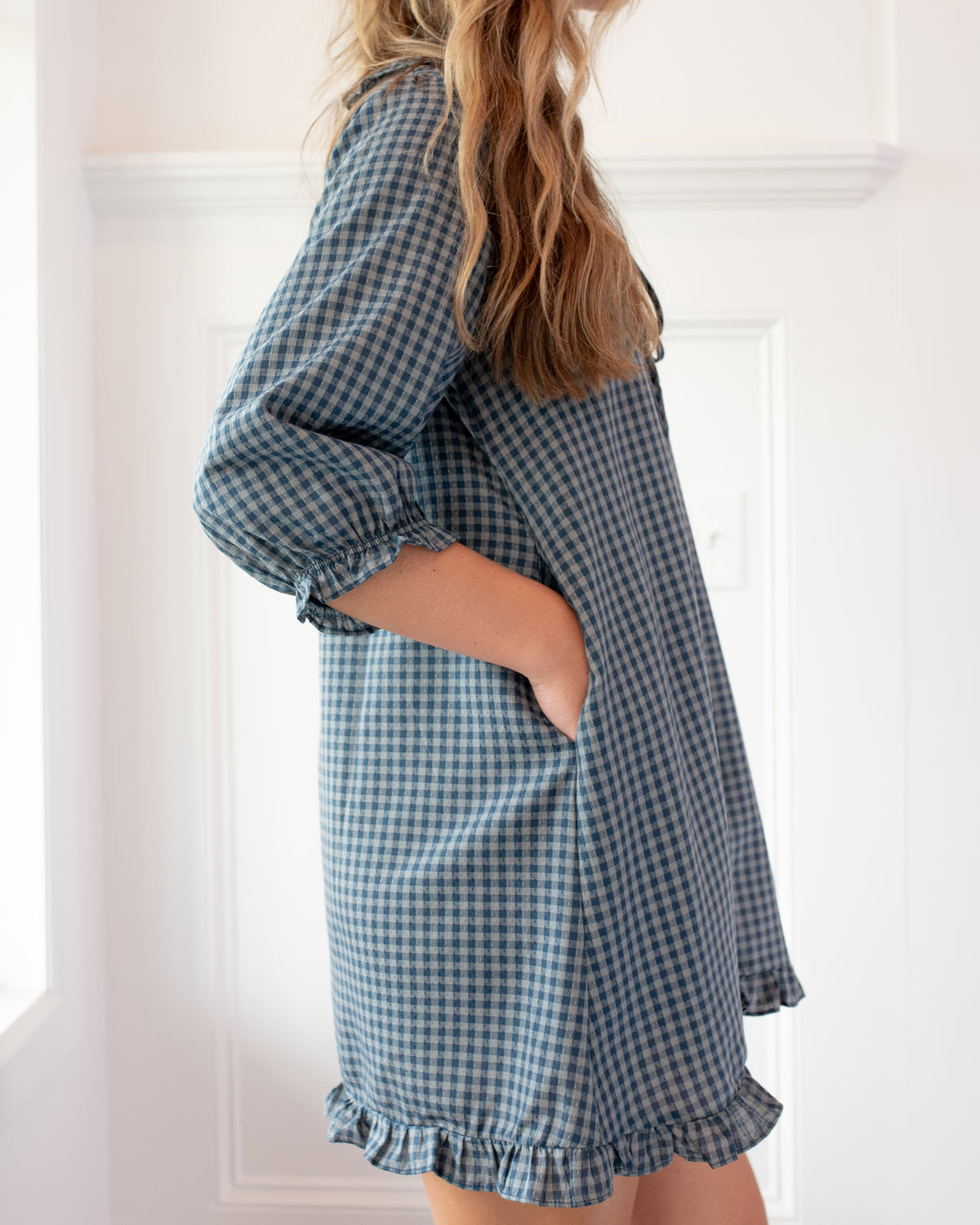 Navy gingham mini dress with hidden side pocket worn by a model, a feminine silhouette, side view.
