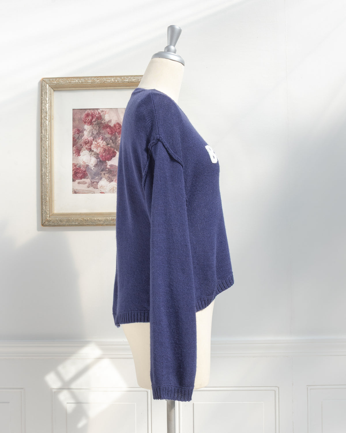 Navy knit sweater with relaxed drop shoulder and ribbed cuffs on a mannequin, classic style, side view.